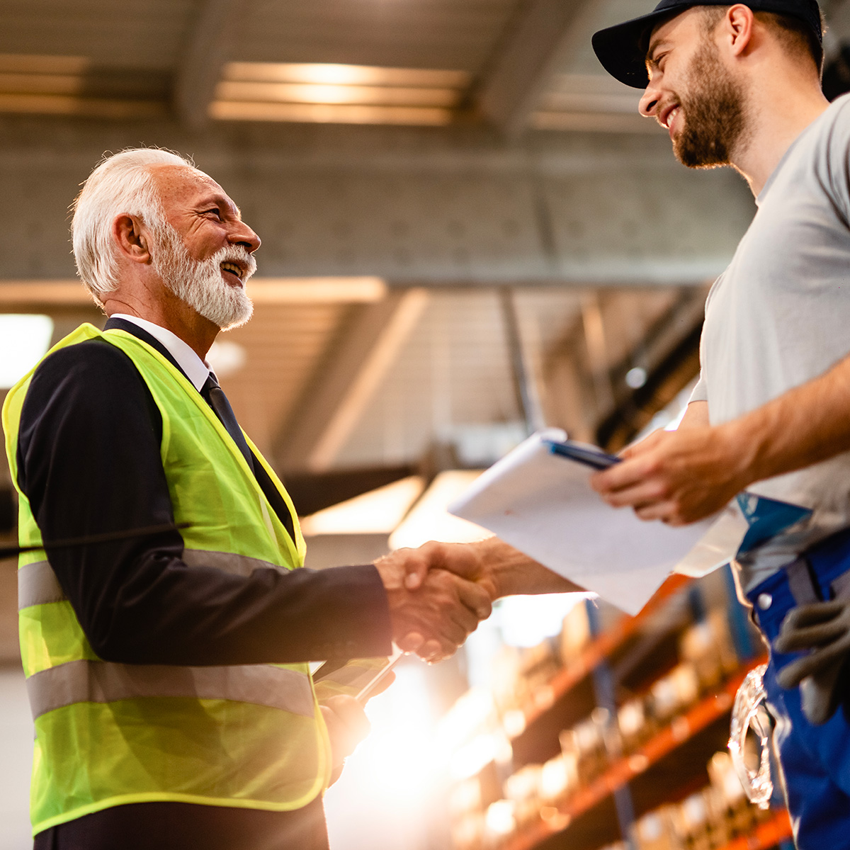 Two men in warehouse setting shaking hands over maintenance agreement