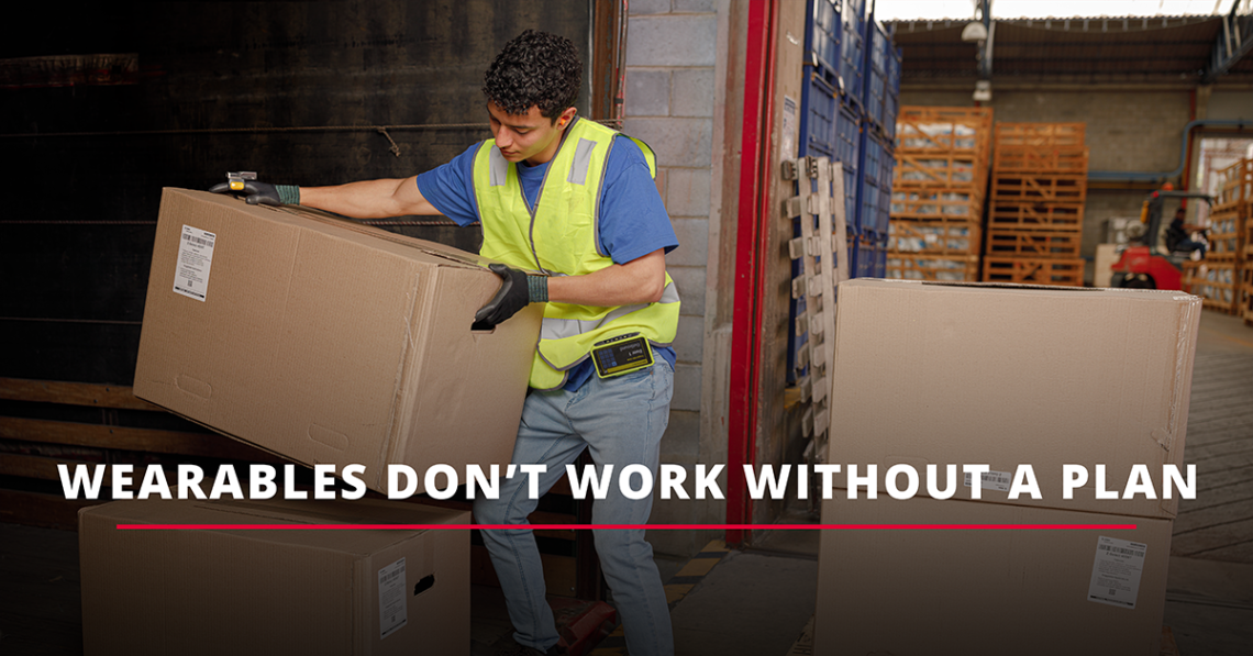 Warehouse worker wearing a Zebra WT6400 wearable computer and RS6100 ring scanner lifts a large cardboard box in a busy loading area. Bold text reads: “Wearables Don’t Work Without a Plan,” with a red underline emphasizing the statement.