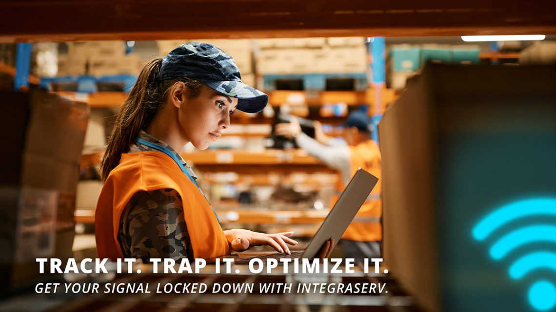 Warehouse employee using a laptop to optimize Wi-Fi signal strength in an industrial setting. Text overlay reads: “Track it. Trap it. Optimize it. Get your signal locked down with IntegraServ.” Promotes Wi-Fi optimization for warehouses with strong connectivity solutions.