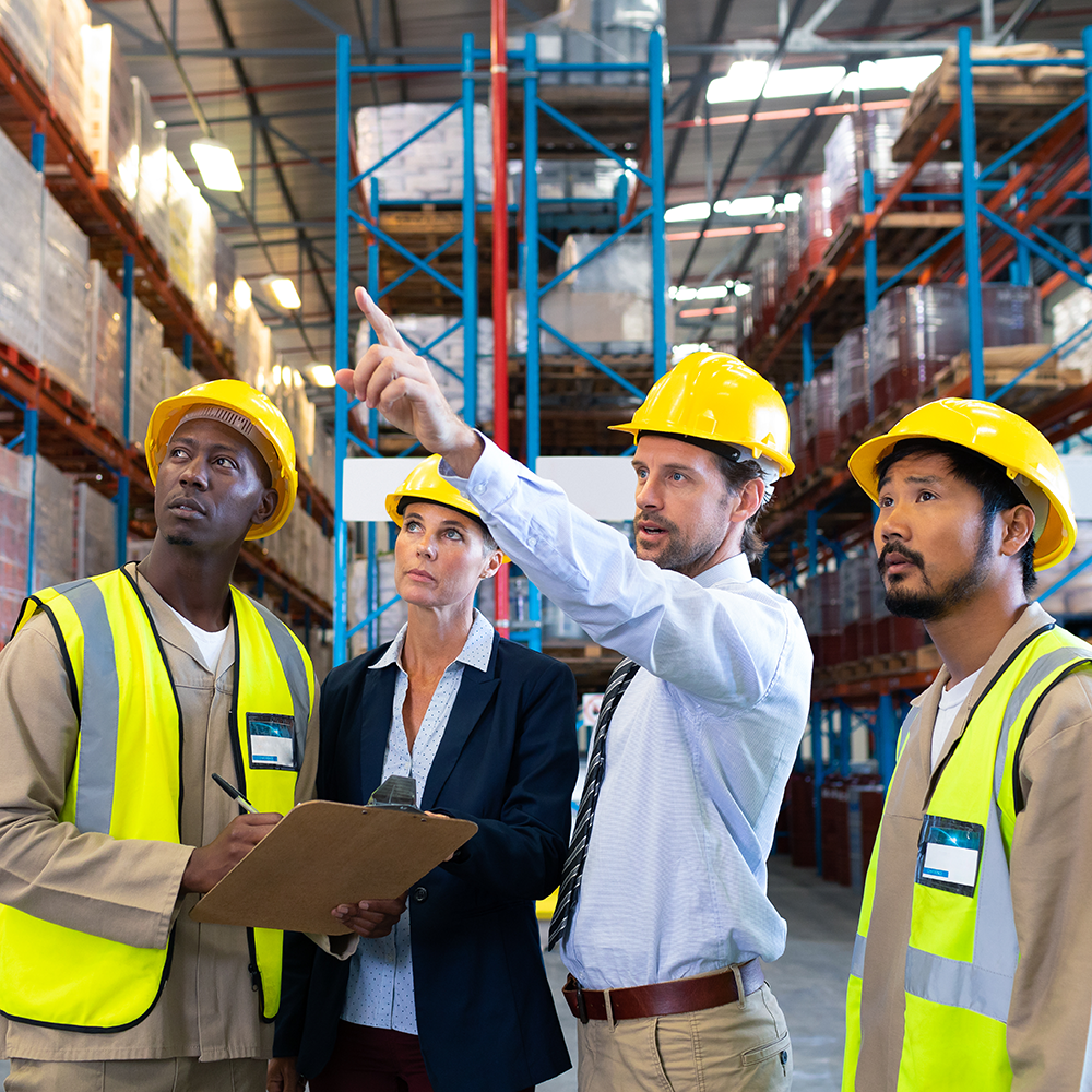 Group of people in a warehouse setting, with one man pointing to a corner of the warehouse