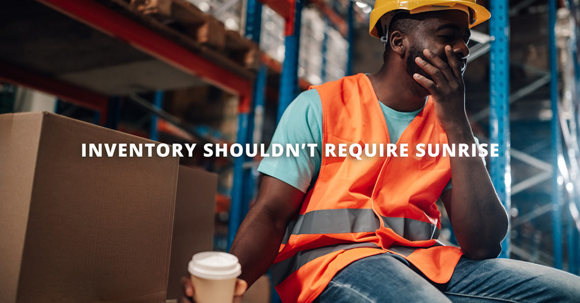 Man holding a cup of coffee in a warehouse setting, wearing a high-vis vest and hard hat, yawning into his other hand. Text overlay reads "inventory shouldn't require sunrise"
